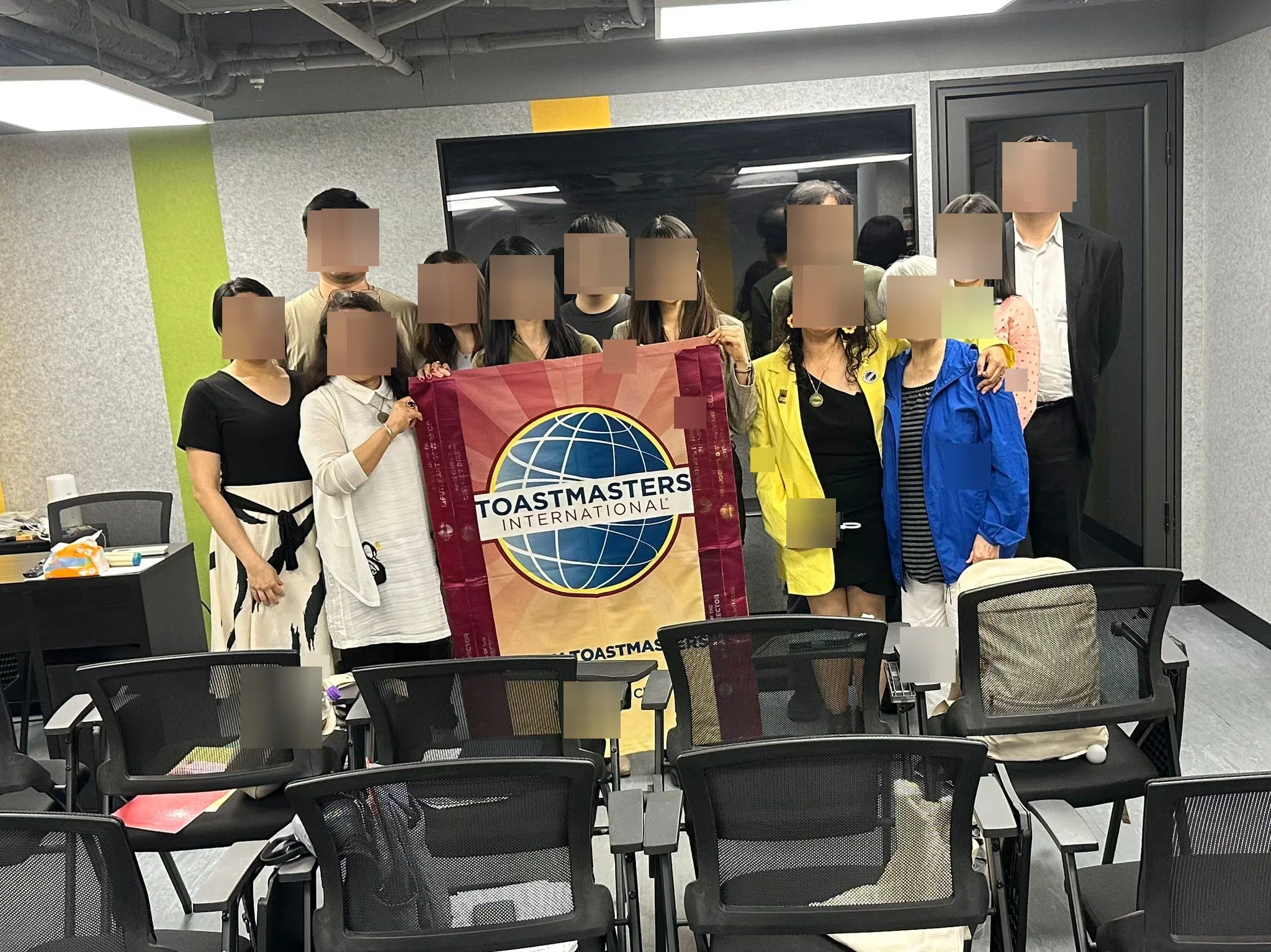 社群活動合照,可見 Toastmasters 旗幟(原相片中的人臉已遮擋) / Community group photo with a Toastmasters banner (faces obscured in the original photo)